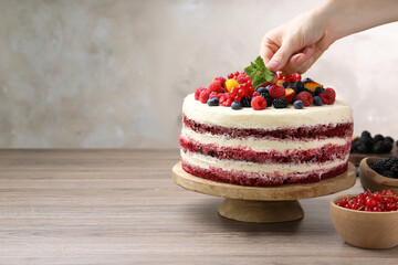 Woman decorating tasty sponge cake with mint at wooden table, closeup. Space for text