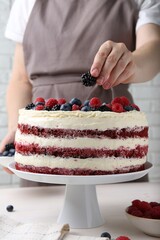 Woman decorating tasty sponge cake with berries at white table, closeup