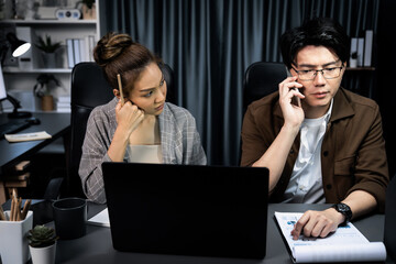 Serious face working on laptop of sales manager calling to customer with secretary writing memo on...