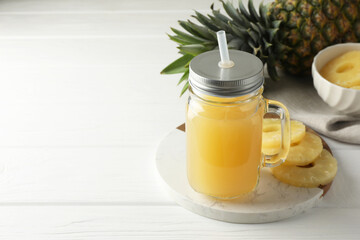 Tasty pineapple juice in mason jar and slices of fresh fruit on white wooden table, closeup. Space for text