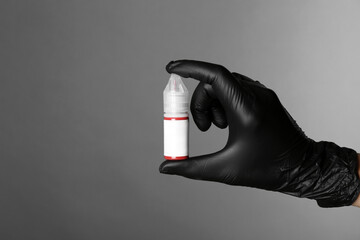 Professional cosmetologist holding bottle of pigment for permanent makeup on grey background,...