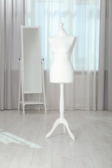 One female mannequin on stand and mirror near window indoors