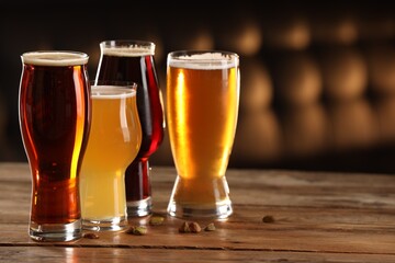 Glasses with different types of beer and pistachio nuts on wooden table indoors, space for text