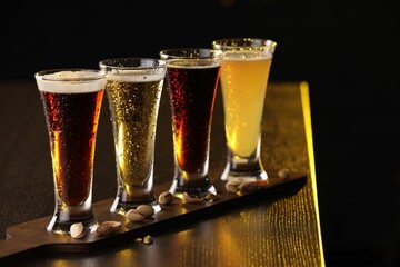 Glasses with different types of beer and pistachios on wooden table against black background, closeup