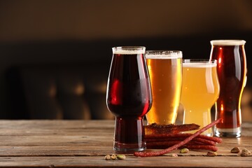 Glasses with different types of beer and snacks on wooden table indoors, space for text