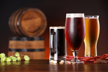 Glasses with different types of beer, snacks and fresh hops on wooden table in bar. Space for text