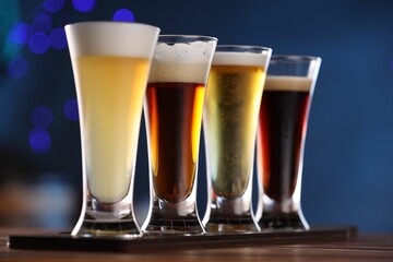Glasses with different types of beer on wooden table against blue background, closeup