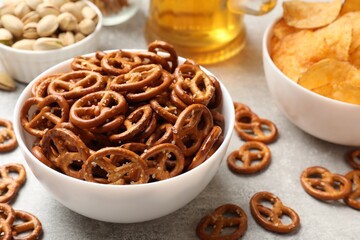 Delicious pretzel crackers, beer and other snacks on light table, closeup