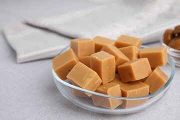 Tasty sweet caramel candies in bowl on light grey table, closeup