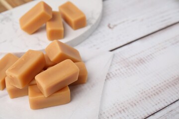 Tasty sweet caramel candies on white wooden table, closeup. Space for text