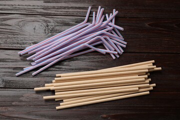 Plastic and bamboo drinking straws on wooden table, flat lay