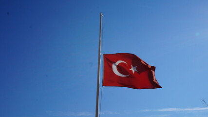 Turkish flag flying at half-mast and fluttering in the wind. Flag against the blue sky. The wind develops a flag