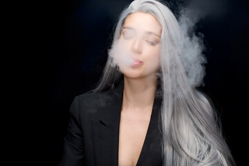 Young woman with long gray hair vaping and exhaling smoke against a dark background, capturing a...