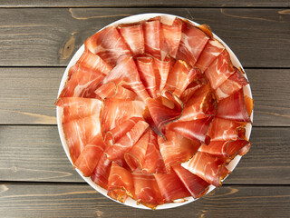 Slices of speck on a plate on the wooden table cured meats raw ham slices of rustic Prosciutto