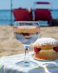 Lunch on sandy beach in Saint-Tropez with cake Tarte tropezienne filled brioche with cream and fresh red berries and glass of rose wine, summer vacation on French riviera, France