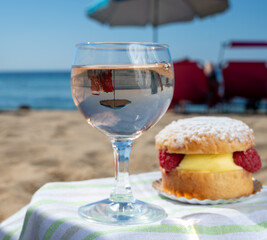 Lunch on sandy beach in Saint-Tropez with cake Tarte tropezienne filled brioche with cream and fresh red berries and glass of rose wine, summer vacation on French riviera, France