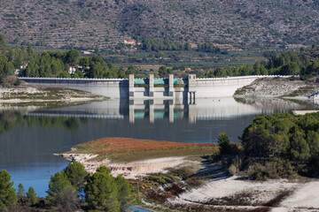 Paisaje con el muro de contención y su reflejo del pantano de Beniarrés donde se aprecia el bajo nivel del agua a causa de la sequía provocada por el cambio climático, España