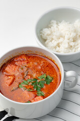 Bowl of curry with pieces of meat and a side of steamed rice arranged neatly for a meal