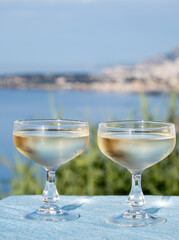 Sparkling wine, cava or champagne in two coupe glasses on table with view on blue sea, Menton and Monte-Carlo, French Riviera, France is summer