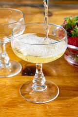 Pouring of brut champagne bubbles wine in coupe glasses and small bowl with fresh strawberries
