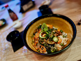 Traditional japanese food in a bowl on a wooden table. Rice with vegetables, seafood and sesame seeds in a bowl with chopsticks