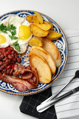 Delicious breakfast plate featuring eggs, beans, bacon, and potato wedges served on a decorative dish