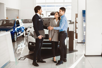 Successful Deal. Car seller handshaking with happy auto buyer couple standing in dealership store, selective focus