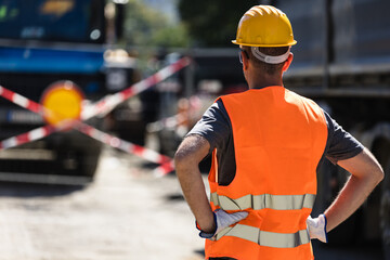 Construction worker observing roadwork barriers during daylight hours while overseeing traffic...