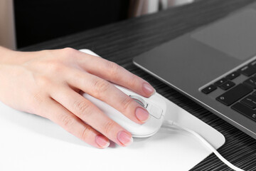 Fototapeta premium Woman using computer mouse while working with laptop at black wooden table, closeup