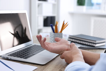 Man suffering from pain in wrist while working on laptop at table indoors, closeup. Carpal tunnel...
