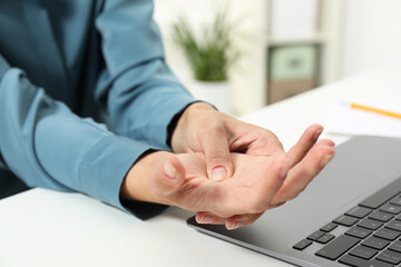 Carpal tunnel syndrome. Woman suffering from pain in wrist at desk indoors, closeup