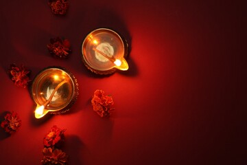 Diwali celebration. Diya lamps and beautiful flowers on red background, flat lay. Space for text