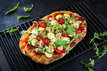 Traditional Italian pinsa bread prosciutto e salsa di pomodoro with tomatoes and zucchini in tomato sauce served as close-up on a rustic cast iron grillage