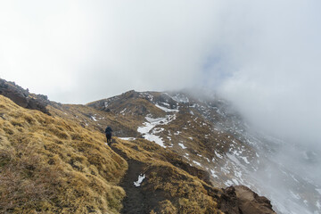 Hiking at volcanic landscape of Mount Etna with black lava and yellow grass on a foggy winter day, Catania, Sicily, Italy