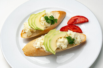 Fresh avocado and cheese spread on toasted bread garnished with cilantro and tomato