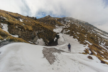 Hiking at snowy volcanic landscape of Mount Etna with black lava and yellow grass on a cloudy winter day, Catania, Sicily, Italy