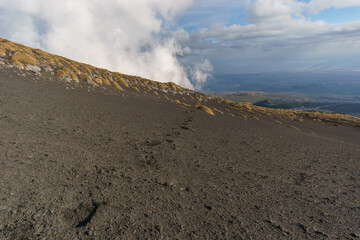 Footprints in ash of the volcanic landscape of Mount Etna with black lava ground and yellow plants of Astragalus siculus, Catania, Sicily, Italy