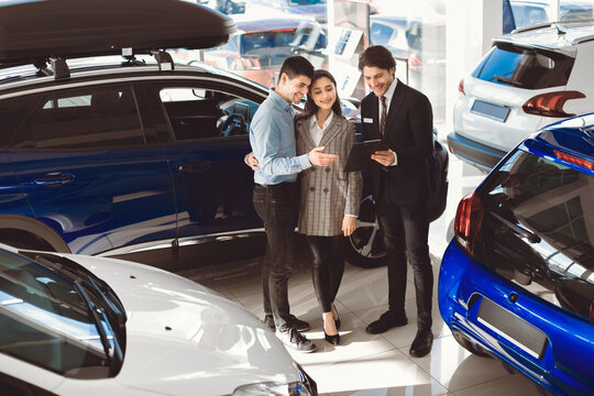 Buy Or Rent Car. Handsome auto vendor with clipboard talking to couple, undersign contract