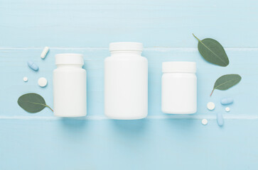 Bottles with pills and green leaves on wooden background, top view