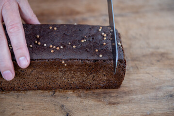 The man cuts whole-wheat rye bread on a wooden cutting board.