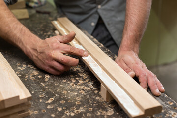 The carpenter smears glue with his finger on an oak part