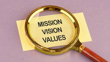 MISSION VISION VALUES symbol. Concept words MISSION VISION VALUES on a yellow business card through a magnifying glass, top view. Concept photo