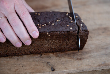 The man cuts whole-wheat rye bread on a wooden cutting board.