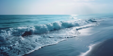 Obraz premium Blue ocean wave crashing gently on the sandy beach under the bright sunlight on a serene summer day