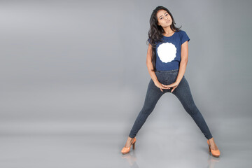 Obraz premium Indian young woman wearing casual t-shirt and jeans, posing sensually with high heel shoe. Footwear advertisement shoot.