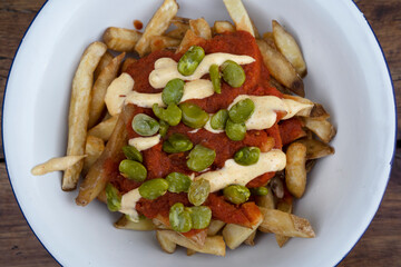 Fried food. Top view of french fries with a spicy sauce and beans, in a white bowl on the table.