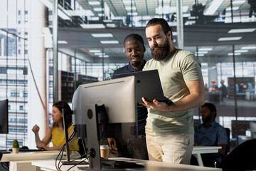 Supervisor looking at laptop screen with employee, showing him key data needed for finding business insights and finishing project task. Company management executives analyzing data on notebook