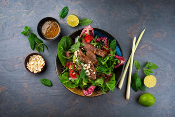 Mixed Thai style green leafy Salad with marinated beef and peanuts served with vinaigrette dressing as top view on a design plate