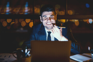 Office Manager Guy Using Voice Assistant On Smartphone Working On Laptop In Modern Office Late At Night. Selective Focus