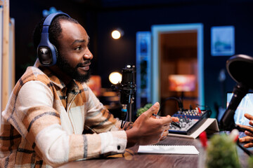 African American guy is speaking into microphone while conducting online radio show. A podcast episode featuring a black man host doing an interview in his home studio for internet audience.